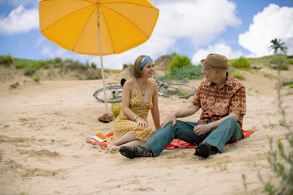 Dos personajes conversan en la playa bajo una sombrilla amarilla en Wild Horse Nine.