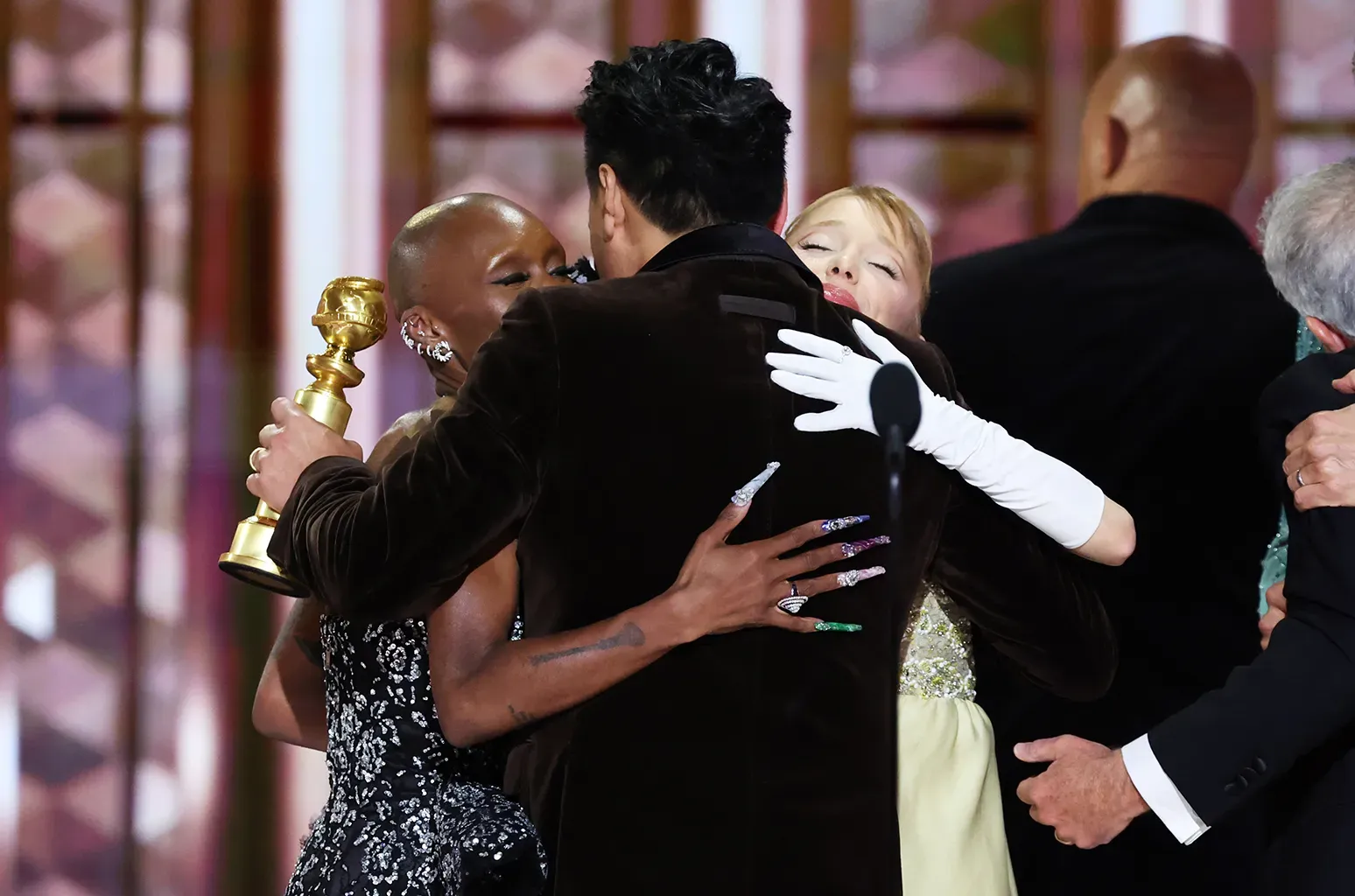 Cynthia Erivo y Ariana Grande abrazando al director Jon M Chu posterior a su discurso al recibir el premio como Mejor Logro Cinematográfico y de Taquilla por "Wicked"